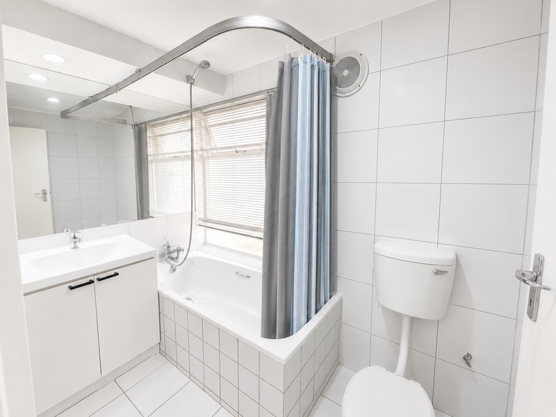 A clean, functional bathroom featuring a built-in vanity, bathtub with shower mixer, wall-mounted toilet, and full-height wall tiling.