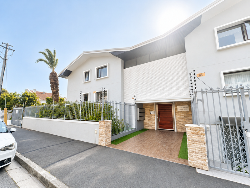 Front elevation of the apartment complex featuring a secure gated entrance, stone-clad accents, modern timber door, and perimeter electric fencing.