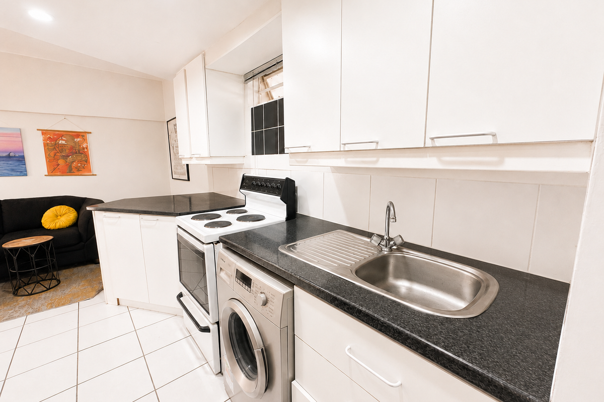 A functional kitchen featuring white cabinetry, black laminate countertops, a stainless steel sink, an electric stove, and a built-in washing machine.