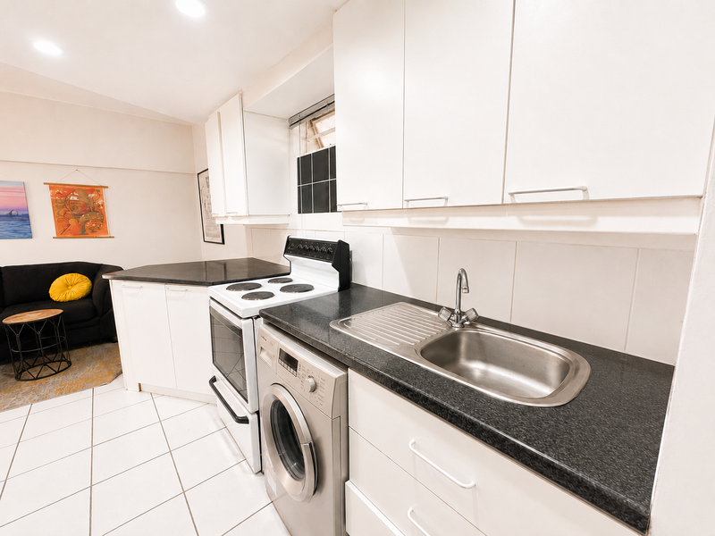 A functional kitchen featuring white cabinetry, black laminate countertops, a stainless steel sink, an electric stove, and a built-in washing machine.