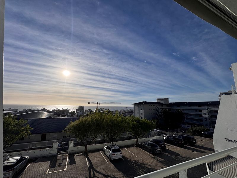An elevated view overlooking a parking area and surrounding urban landscape towards the ocean.