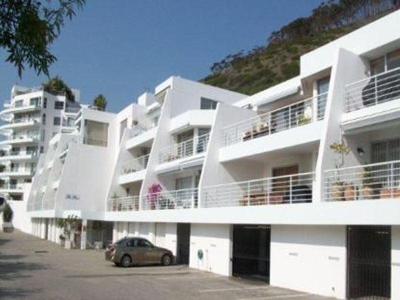 A multi-story apartment complex featuring white facade, private balconies with metal railings, and ground-level garage access.