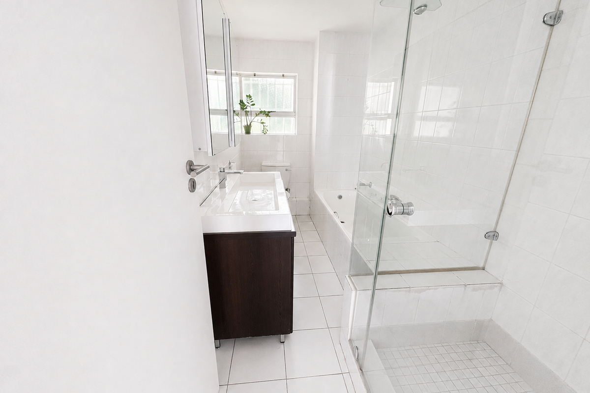 A clean, bright bathroom featuring a glass-enclosed shower, a built-in bathtub, a modern vanity with an integrated sink, and neutral white tiled finishes.
