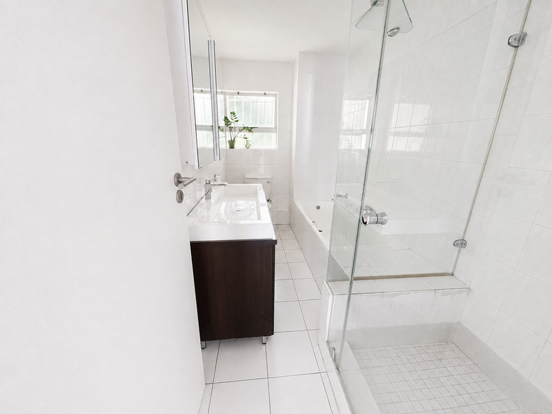 A clean, bright bathroom featuring a glass-enclosed shower, a built-in bathtub, a modern vanity with an integrated sink, and neutral white tiled finishes.