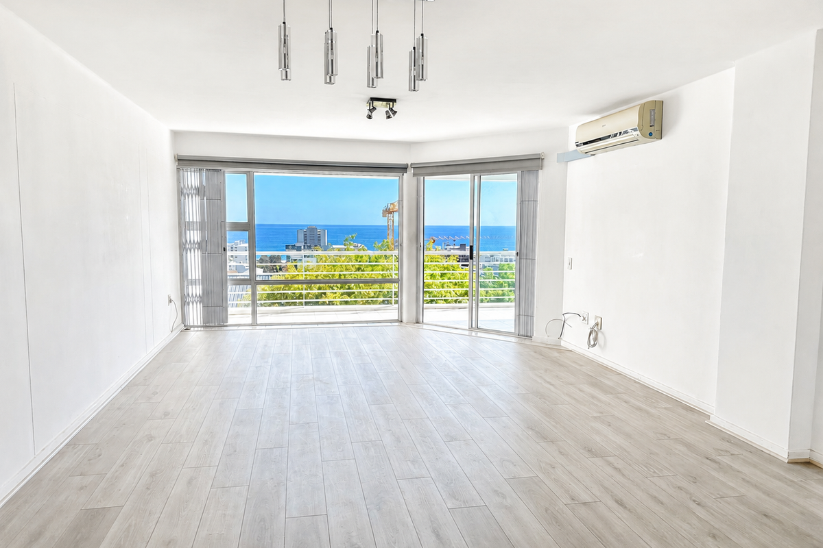 Spacious, light-filled living area featuring modern laminate flooring, split-system air conditioning, and large sliding doors opening to a balcony with ocean views.