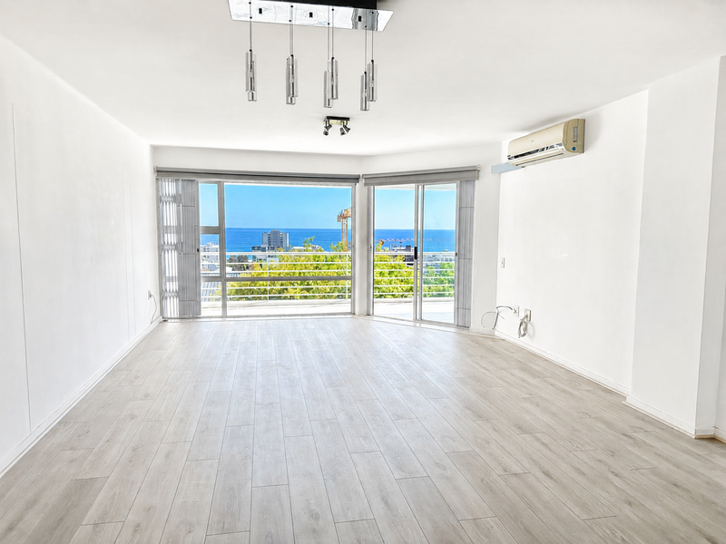 Spacious, light-filled living area featuring modern laminate flooring, split-system air conditioning, and large sliding doors opening to a balcony with ocean views.
