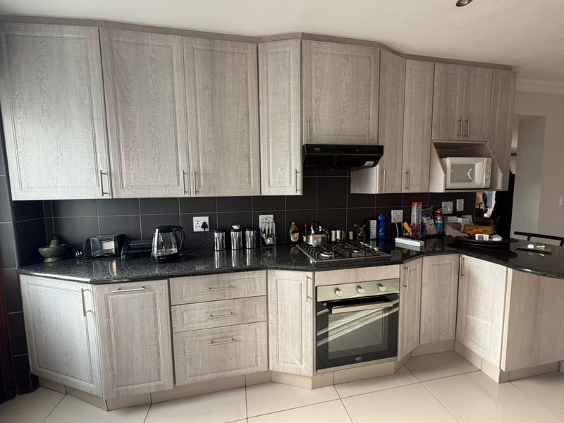 Modern kitchen featuring light wood-grain cabinetry, dark granite countertops, a gas hob, built-in oven, and integrated microwave with a sleek tiled backsplash.