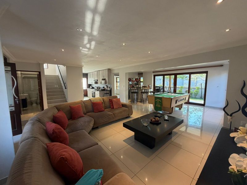 Spacious open-plan living area featuring tiled floors, recessed lighting, and seamless flow to the kitchen and outdoor patio through large sliding glass doors.