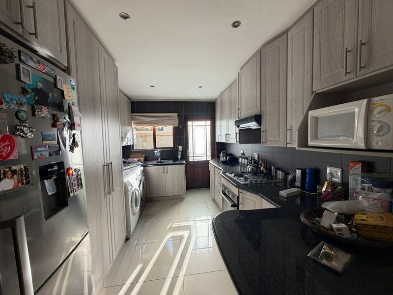 A functional galley-style kitchen featuring light wood-grain cabinetry, dark granite countertops, integrated gas hob, and tiled flooring with direct access to the rear exterior.