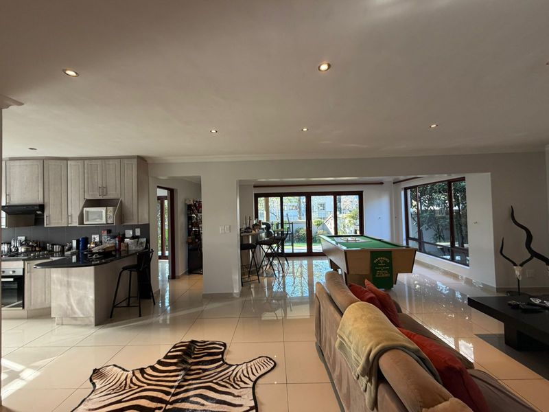 Spacious open-plan living area featuring a modern kitchen with granite countertops, tiled flooring, recessed lighting, and large sliding doors leading to the outdoors.