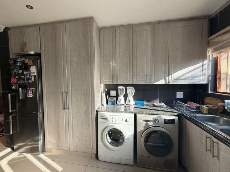 A functional laundry area featuring modern wood-grain cabinetry, granite countertops, a stainless steel sink, and tiled finishes with dedicated space for appliances.