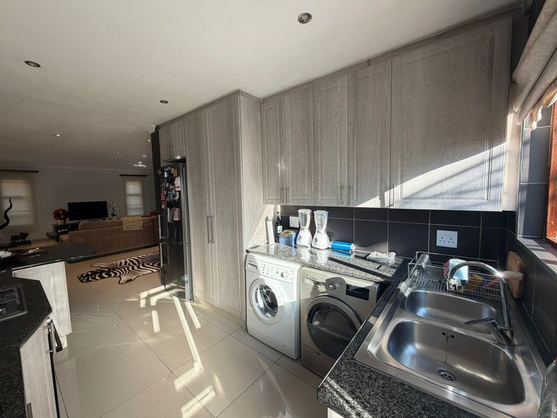 Open-plan kitchen area featuring modern grey cabinetry, granite countertops, a double stainless steel sink, and integrated laundry appliances, flowing into the living space.