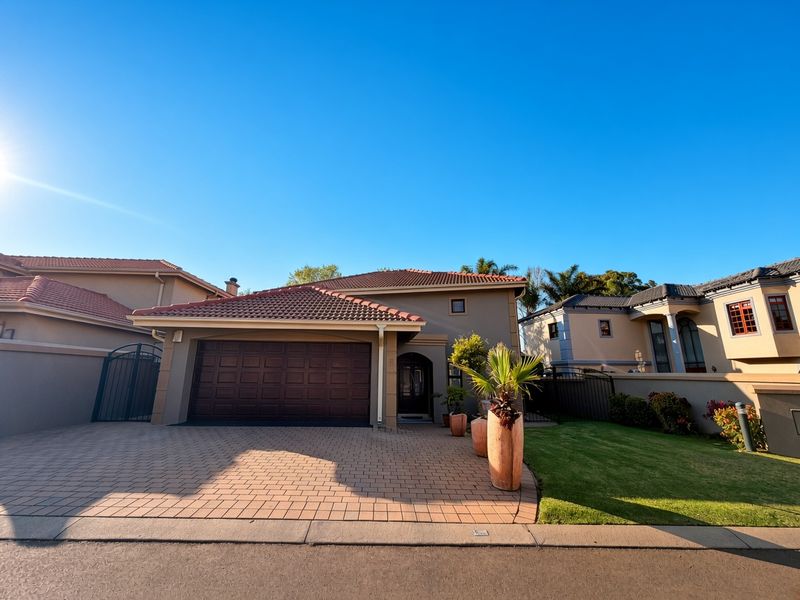 Front elevation of a residential house featuring a paved driveway, double garage, and tiled roof, set within a well-maintained suburban estate.