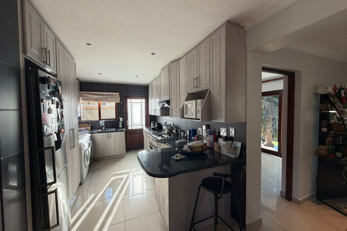 Modern kitchen featuring light wood cabinetry, dark granite countertops, gas hob, built-in microwave, and tiled flooring with direct access to the rear garden.