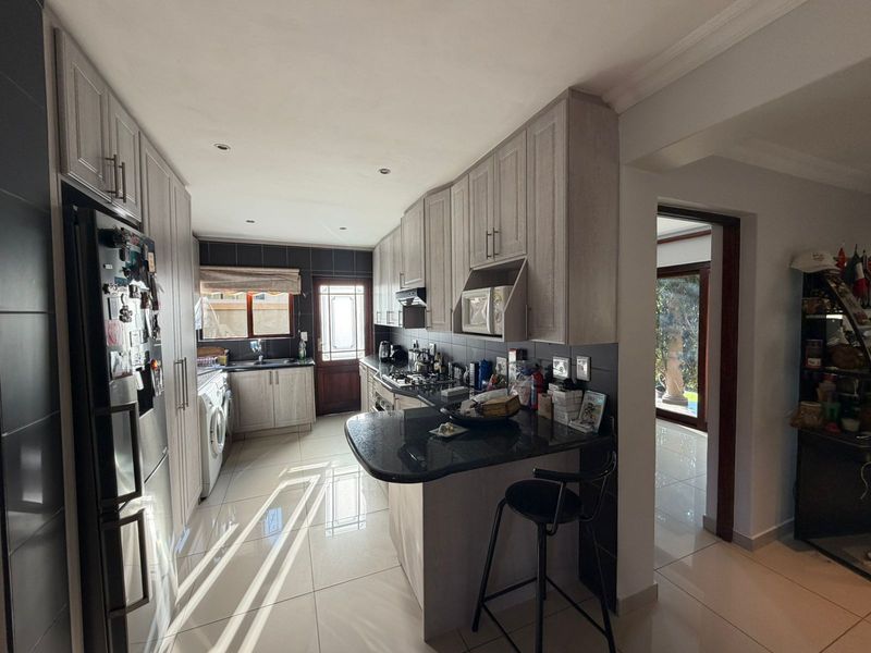 Modern kitchen featuring light wood cabinetry, dark granite countertops, gas hob, built-in microwave, and tiled flooring with direct access to the rear garden.