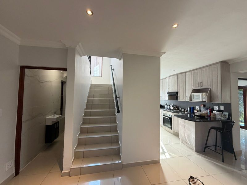 Open-plan living area featuring a tiled staircase with a modern handrail, adjacent to a well-appointed kitchen with granite countertops and built-in appliances.