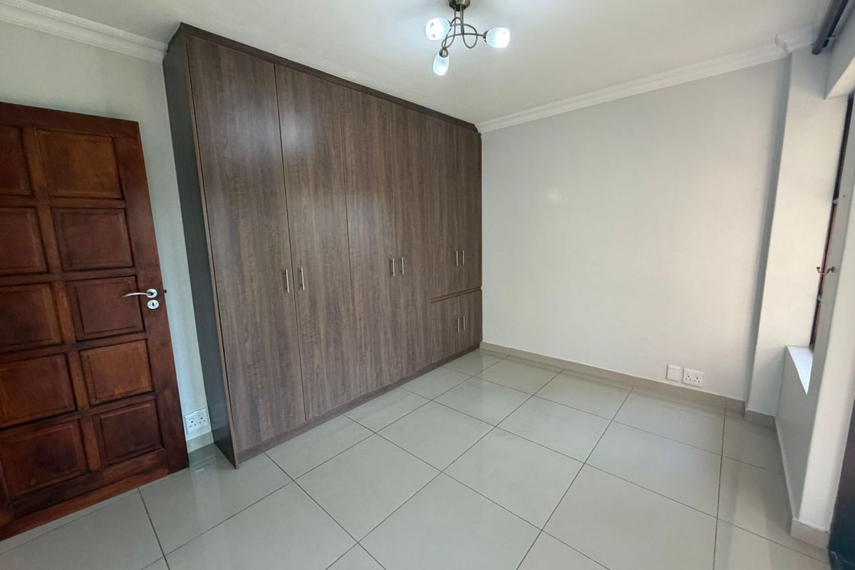 A clean, empty bedroom featuring modern wood-finish built-in cupboards, neutral tiled flooring, and a classic timber door.
