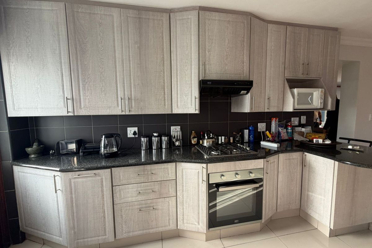 Modern kitchen featuring light wood-grain cabinetry, dark granite countertops, a gas hob, built-in oven, and integrated microwave with a sleek tiled backsplash.