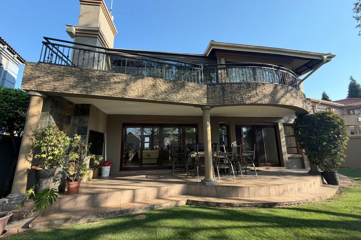 Spacious rear patio featuring stone cladding, tiled flooring, and a large upper-level balcony with wrought iron railings, overlooking the garden.