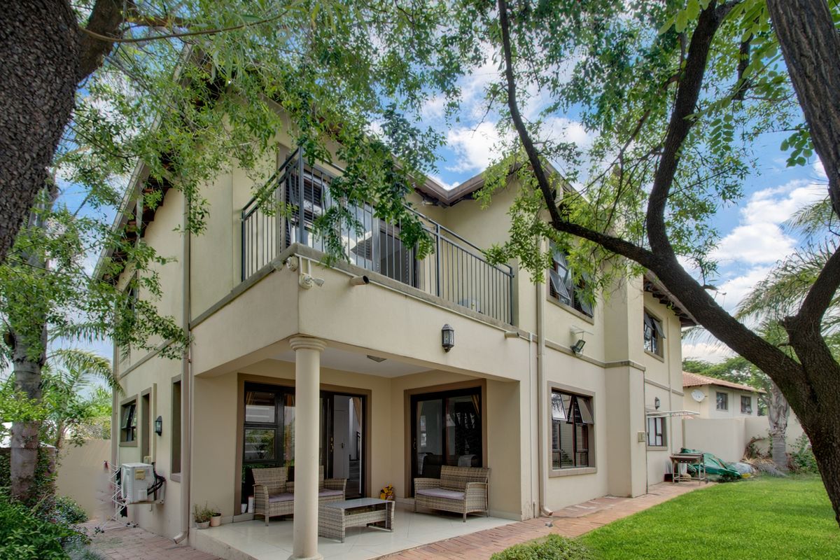 Rear view of the house featuring a covered patio, an upper-level balcony with metal railings, and a well-maintained garden with brick paving.
