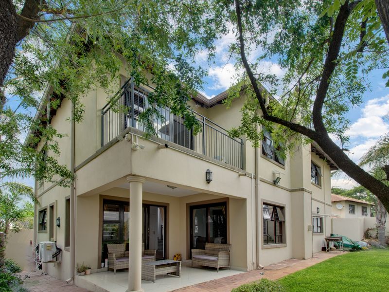Rear view of the house featuring a covered patio, an upper-level balcony with metal railings, and a well-maintained garden with brick paving.