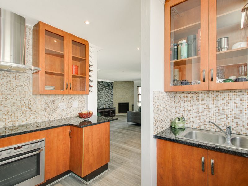 A functional kitchen featuring wooden cabinetry, granite countertops, mosaic tile backsplash, and built-in appliances, with an open flow into the adjacent living area.