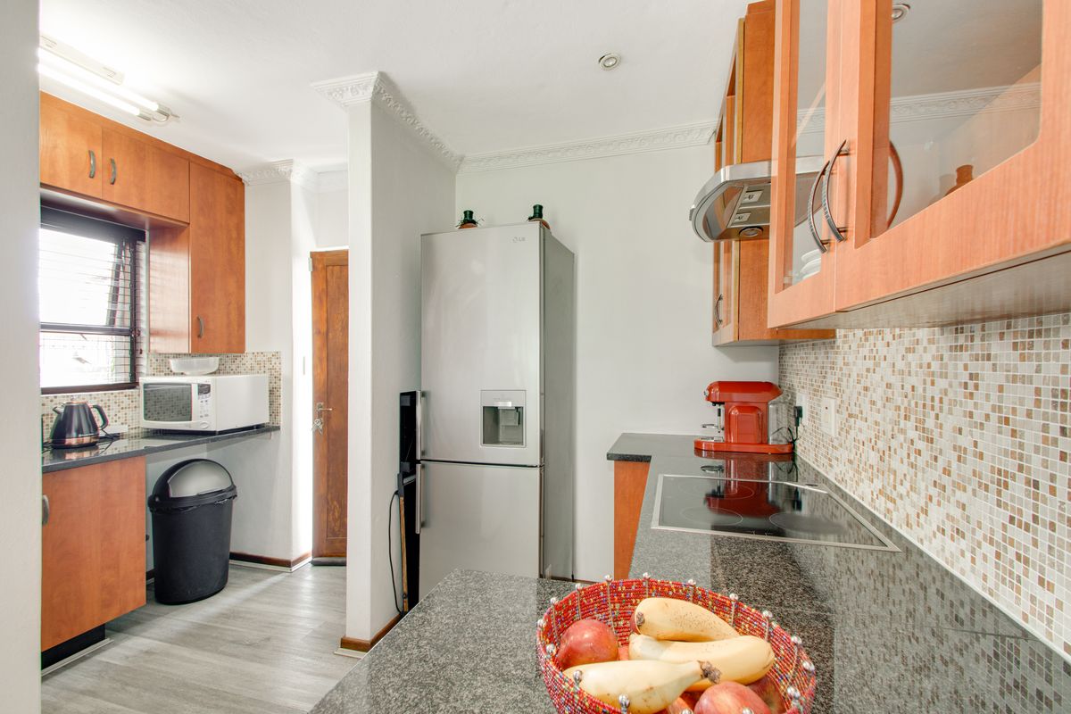 A functional kitchen featuring granite countertops, mosaic tile backsplash, built-in wooden cabinetry, and a glass-top hob with an integrated extractor fan.