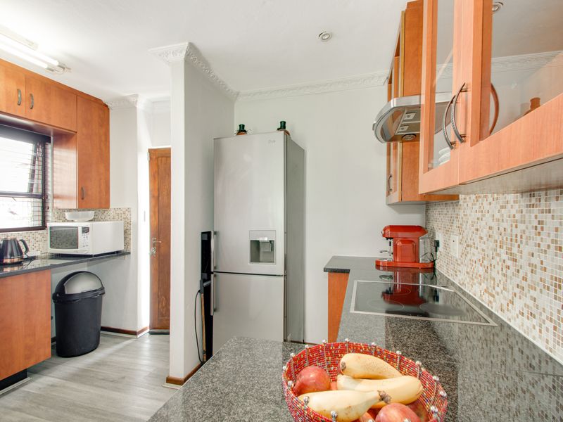 A functional kitchen featuring granite countertops, mosaic tile backsplash, built-in wooden cabinetry, and a glass-top hob with an integrated extractor fan.