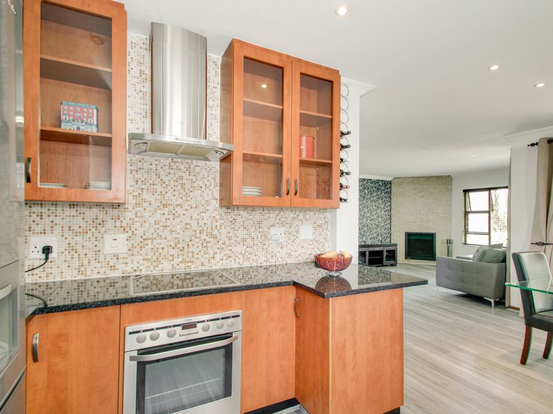 Open-plan kitchen featuring wood-finish cabinetry, granite countertops, and a mosaic backsplash, flowing into a living area with a fireplace and modern laminate flooring.