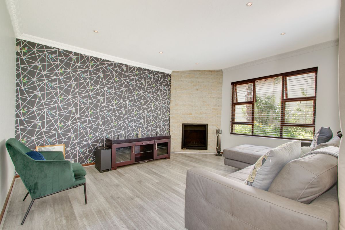 A well-maintained living room featuring a corner fireplace with stone cladding, recessed downlights, crown molding, and modern timber-look laminate flooring.
