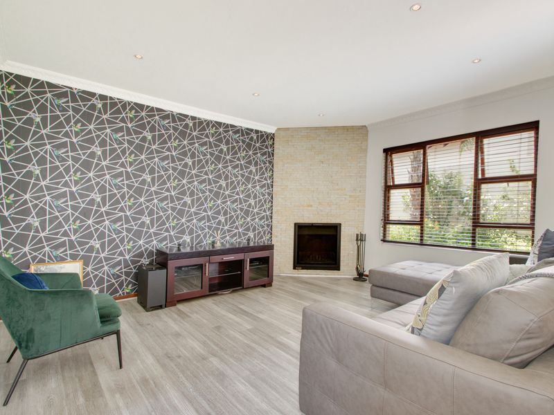 A well-maintained living room featuring a corner fireplace with stone cladding, recessed downlights, crown molding, and modern timber-look laminate flooring.