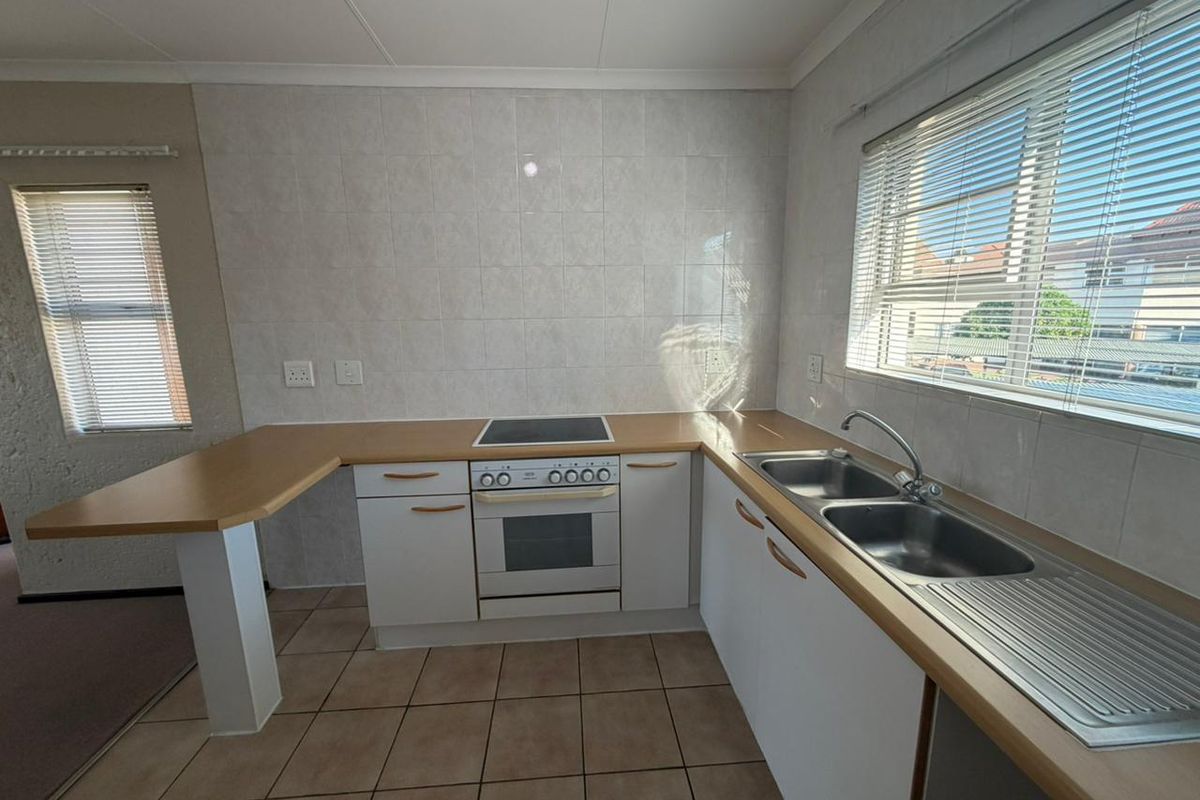 A functional kitchen featuring built-in cabinetry, a double stainless steel sink, an electric oven with hob, and tiled splashbacks with neutral flooring.