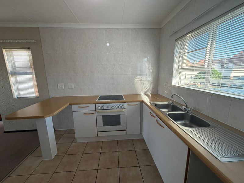 A functional kitchen featuring built-in cabinetry, a double stainless steel sink, an electric oven with hob, and tiled splashbacks with neutral flooring.