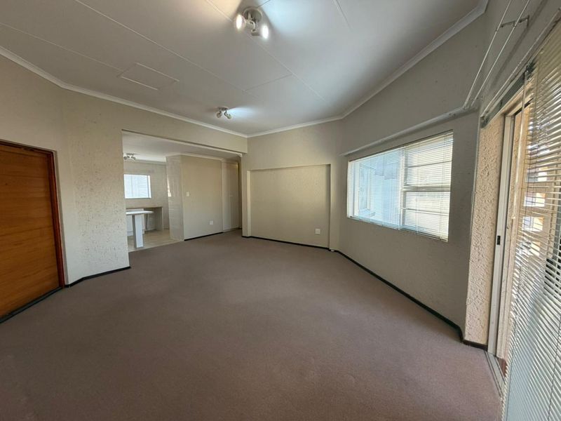 Spacious open-plan living area featuring neutral textured walls, carpet flooring, and a sliding glass door with venetian blinds leading to an outdoor space.