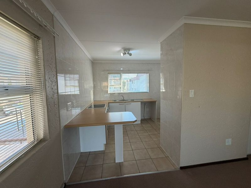 A functional, empty kitchen featuring tiled flooring, laminate countertops, built-in cabinetry, and a built-in hob, offering a clean canvas for potential updates.