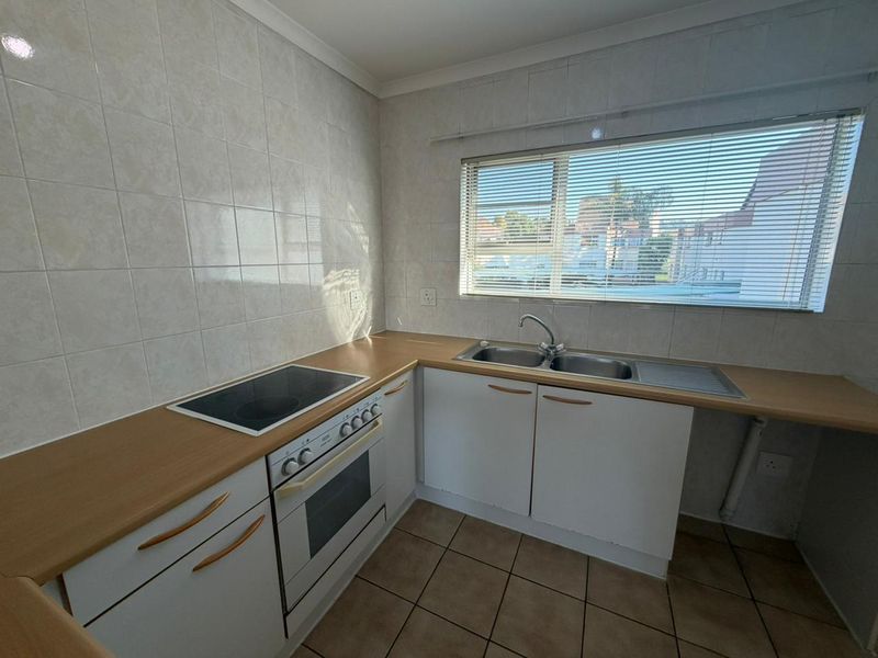 A functional kitchen featuring built-in cabinetry, an electric oven and hob, double sink, and tiled splashbacks with neutral finishes.