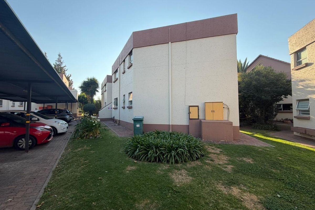 Exterior view of the apartment building featuring a paved driveway, covered carport parking, and surrounding landscaped garden areas.