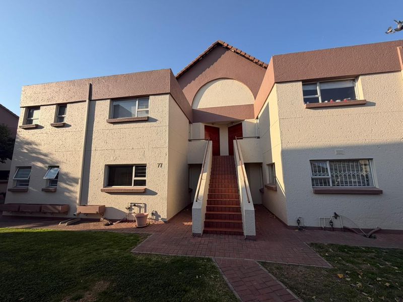 Front elevation of a two-story apartment building featuring a central staircase, textured facade, and paved entrance area.