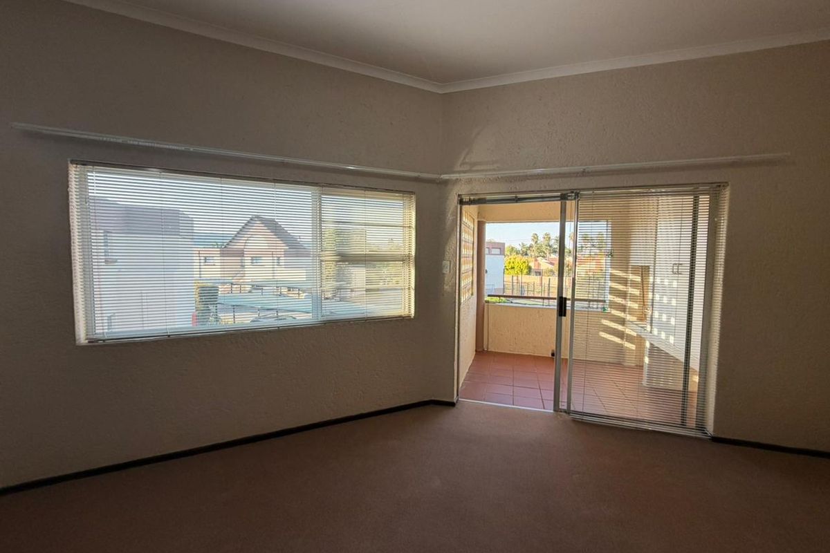 An empty living room featuring carpeted flooring, textured walls, and a sliding glass door providing access to a private balcony.