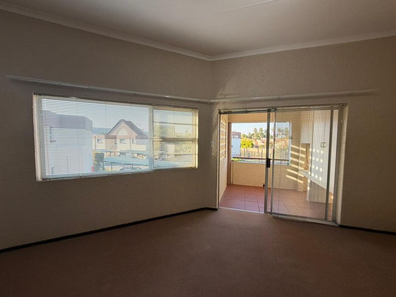 An empty living room featuring carpeted flooring, textured walls, and a sliding glass door providing access to a private balcony.