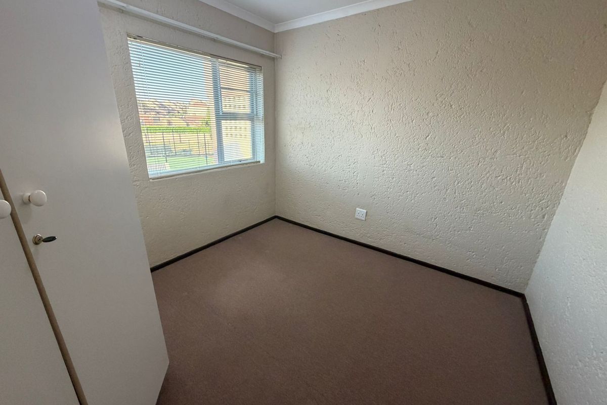 An empty bedroom featuring textured walls, carpeted flooring, and a built-in cupboard, offering a blank canvas for potential updates and interior design.