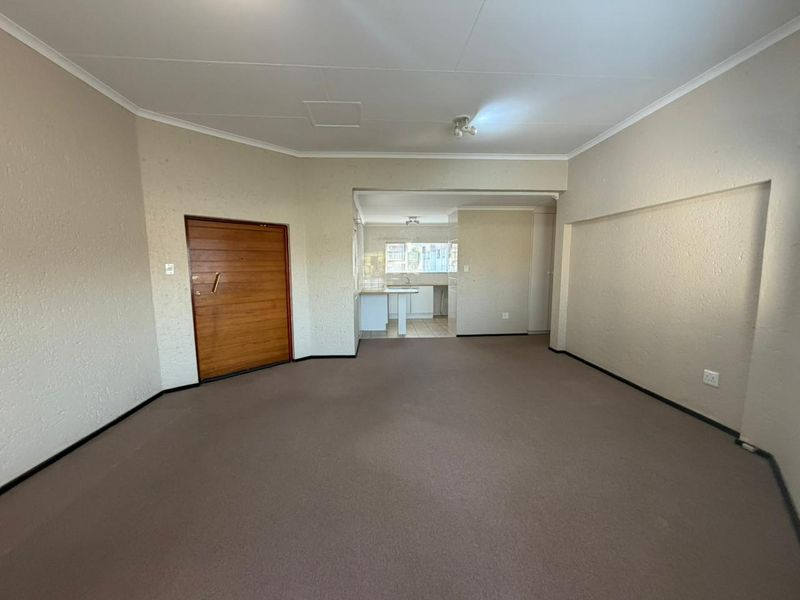 Spacious open-plan living area featuring carpeted flooring and a direct view into the kitchen, offering a blank canvas for renovation.