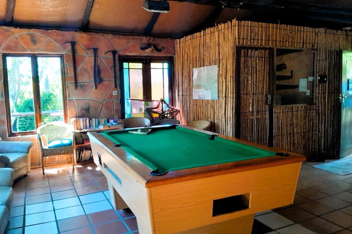 A rustic living area featuring exposed timber ceiling beams, stone wall cladding, and tiled flooring, currently set up as a recreational space.
