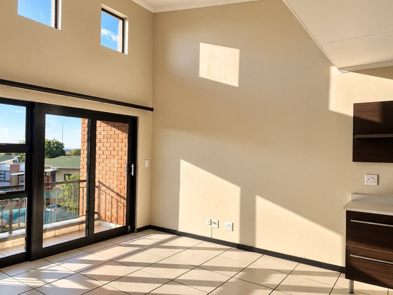 Bright open-plan living area featuring high ceilings, tiled floors, and large sliding doors leading to a balcony, with built-in cabinetry.