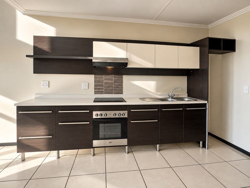 Modern kitchen featuring dark wood and cream cabinetry, integrated electric hob and oven, stainless steel sink, and neutral tiled flooring.