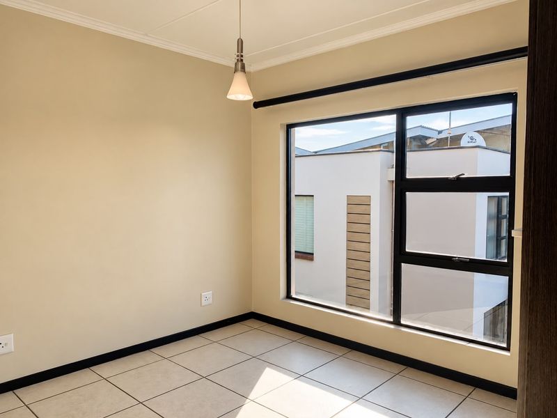 A bright, empty bedroom featuring neutral walls, tiled flooring, and large windows with black frames, offering a clean and well-maintained space.