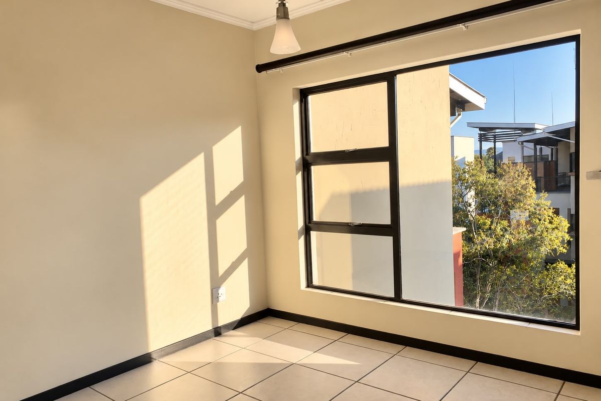 A bright, empty bedroom featuring neutral walls, tiled flooring, and a large window providing natural light and an exterior view.