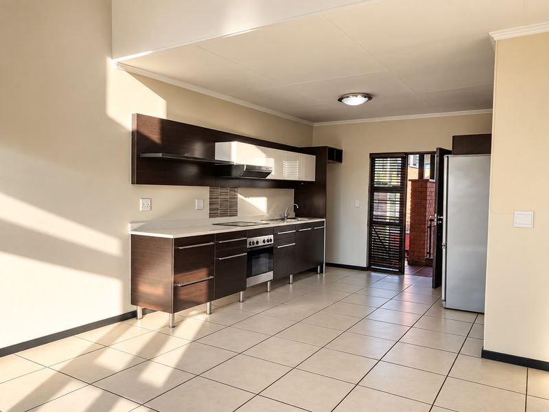 Modern kitchen featuring dark wood cabinetry, built-in oven and hob, tiled flooring, and direct access to an outdoor balcony area.