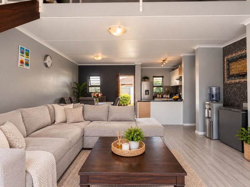 An open-plan living and kitchen area featuring modern laminate flooring, neutral grey walls, and a functional kitchen layout with built-in cabinetry.