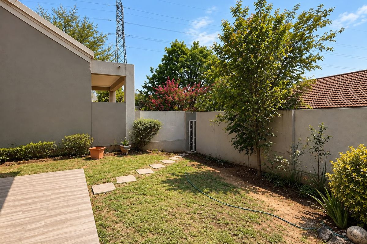 A private rear garden featuring a tiled patio area, perimeter boundary wall with a pedestrian gate, and established garden greenery.